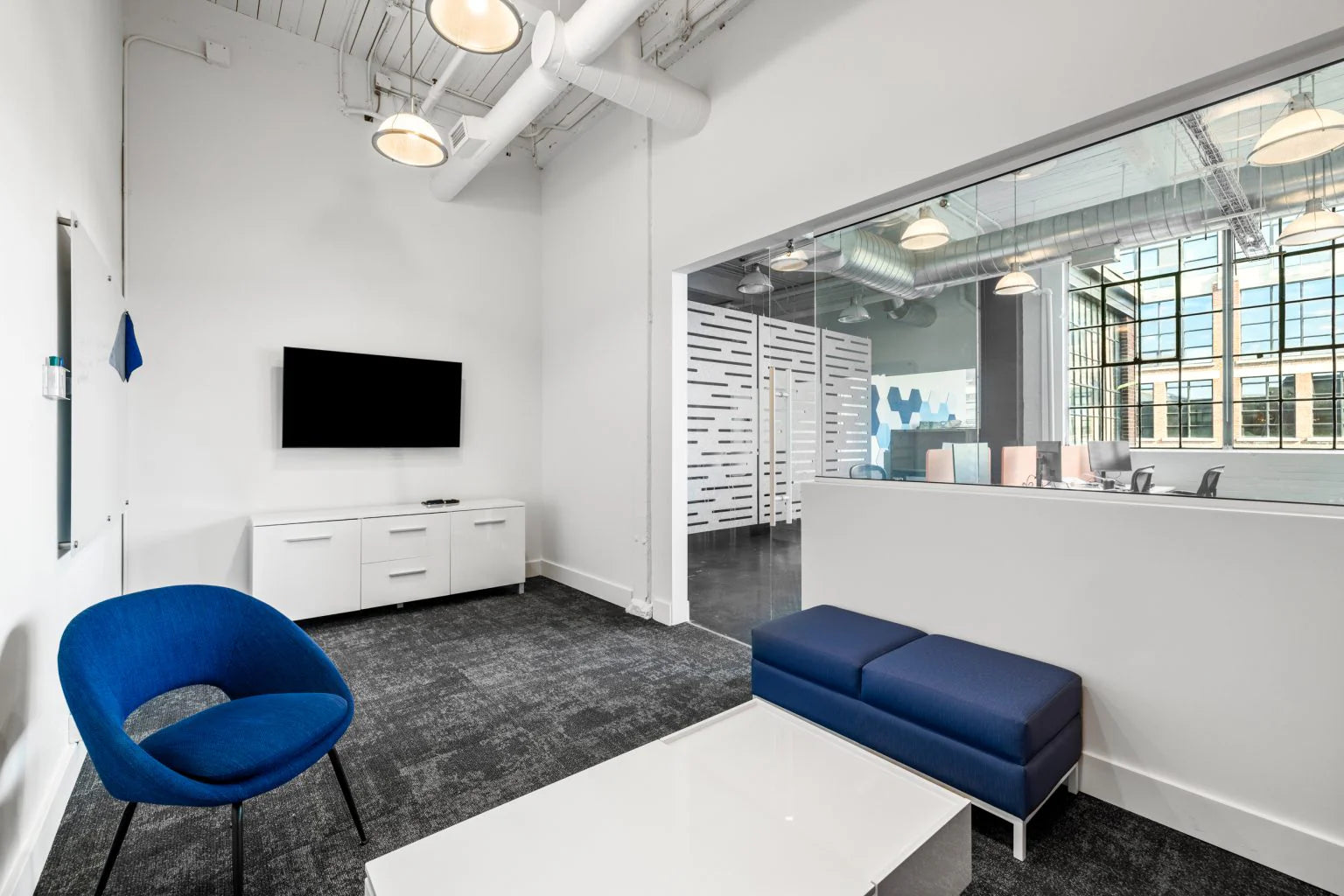 Modern office space with blue chairs and a TV on a white wall.