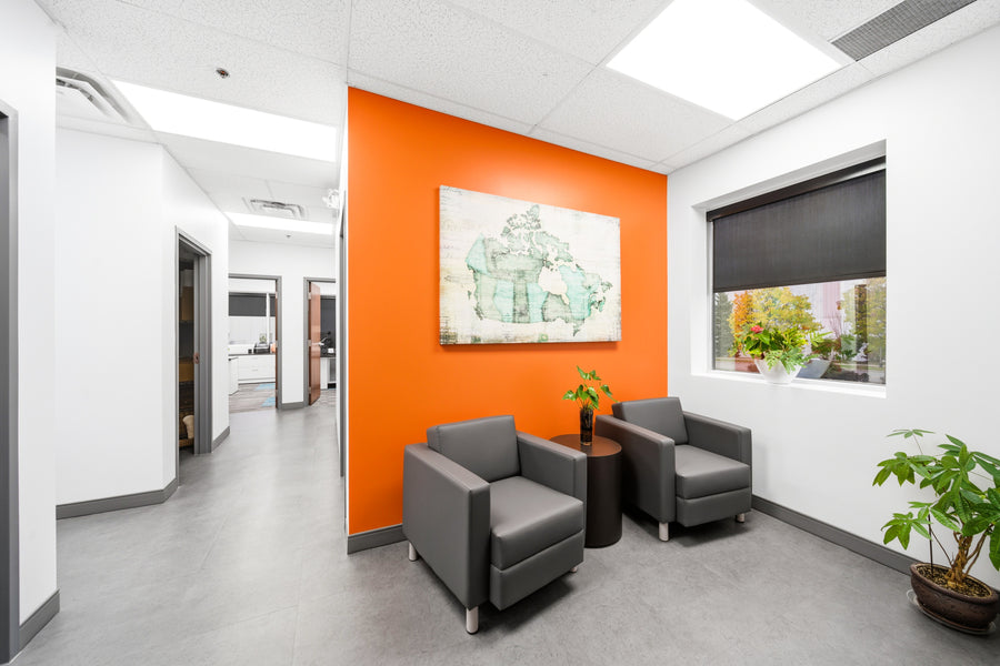 Modern office waiting area with orange wall, gray chairs, and decorative plants.