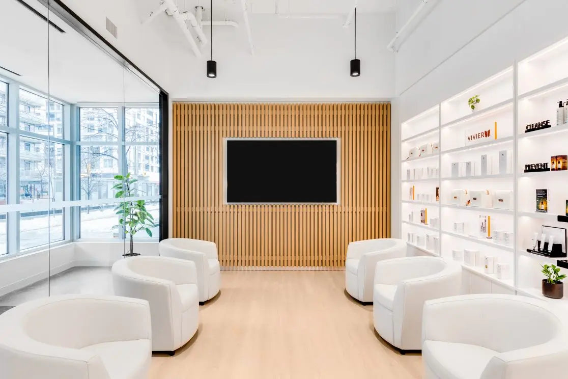 Modern waiting room with white chairs, a television on a wooden panel, and shelves with books.