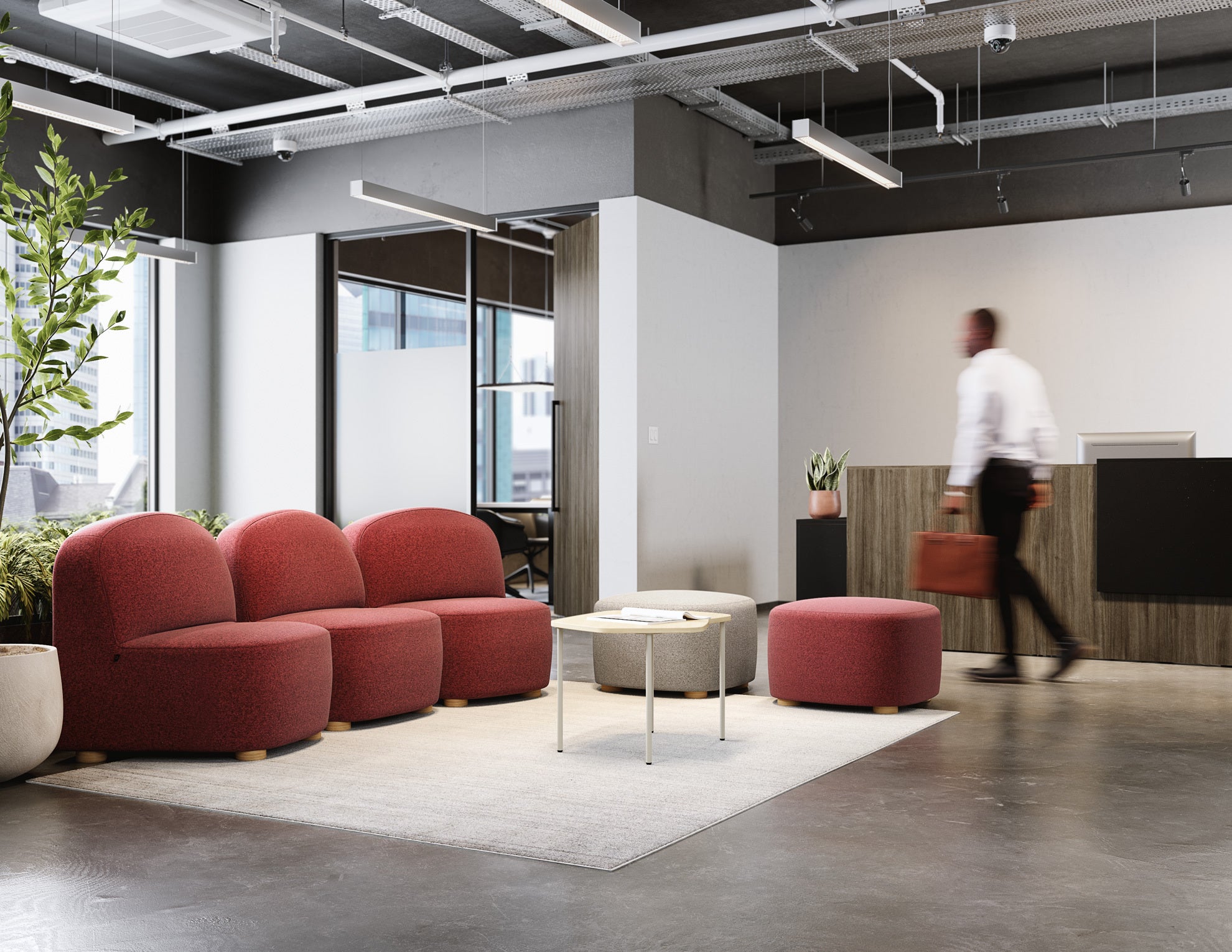 Modern office space with red couches, a coffee table, and a person walking in the background.