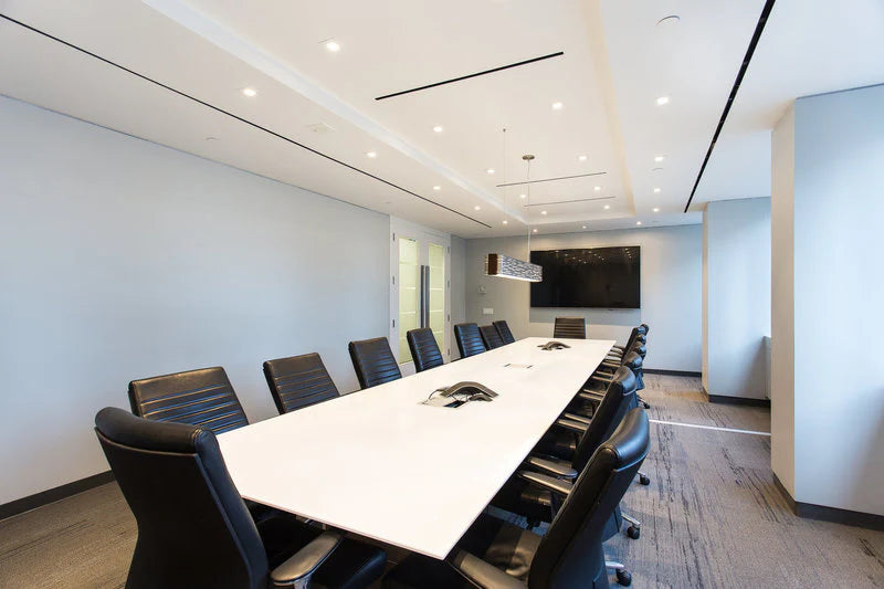 Modern conference room with a long white table and black chairs.