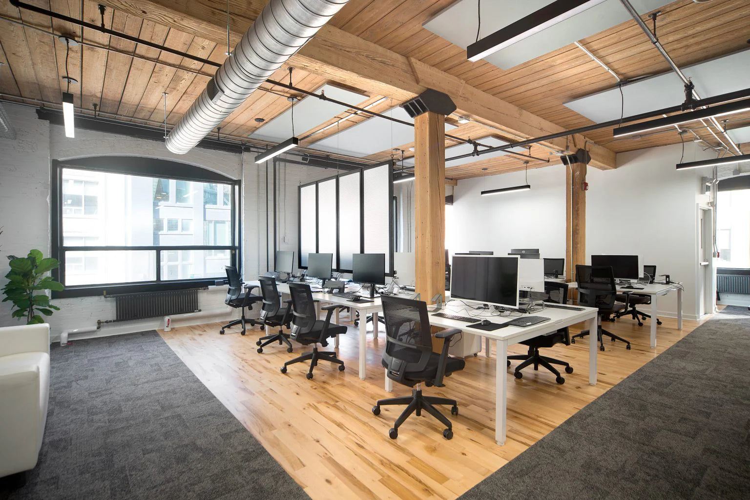Modern office space with wooden floors, large windows, and office furniture.