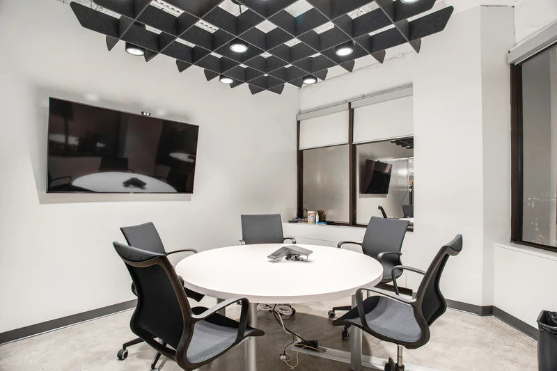 Modern conference room with round table and chairs, featuring a large screen on the wall.