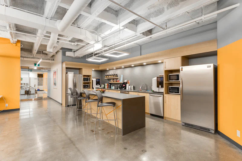 Modern kitchen with stainless steel appliances and wooden cabinets in a bright office setting.