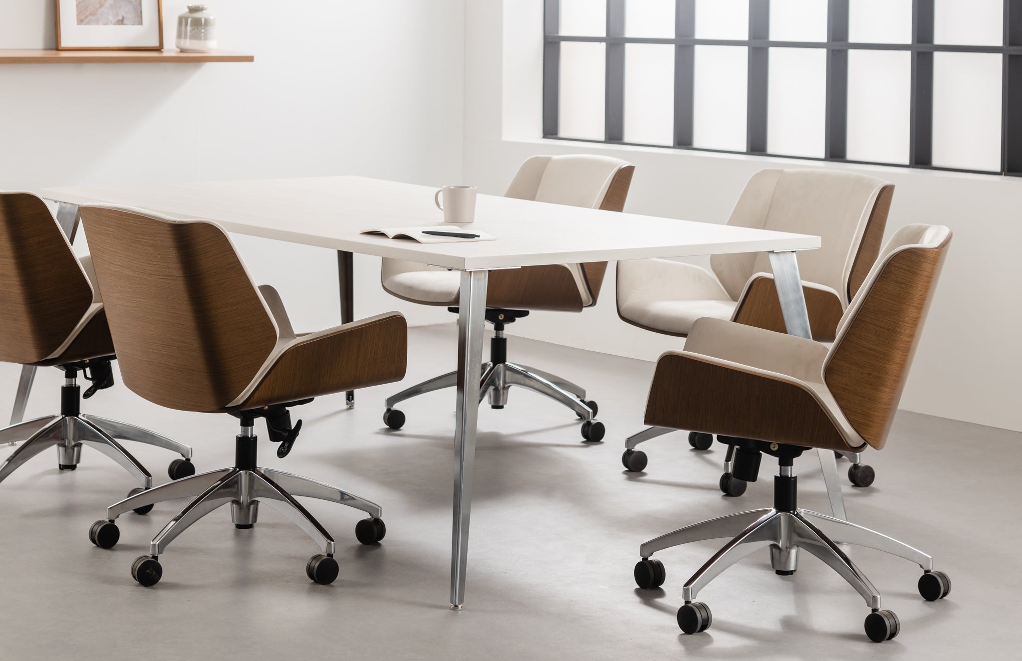 Modern office chairs around a white table in a bright room with large windows.